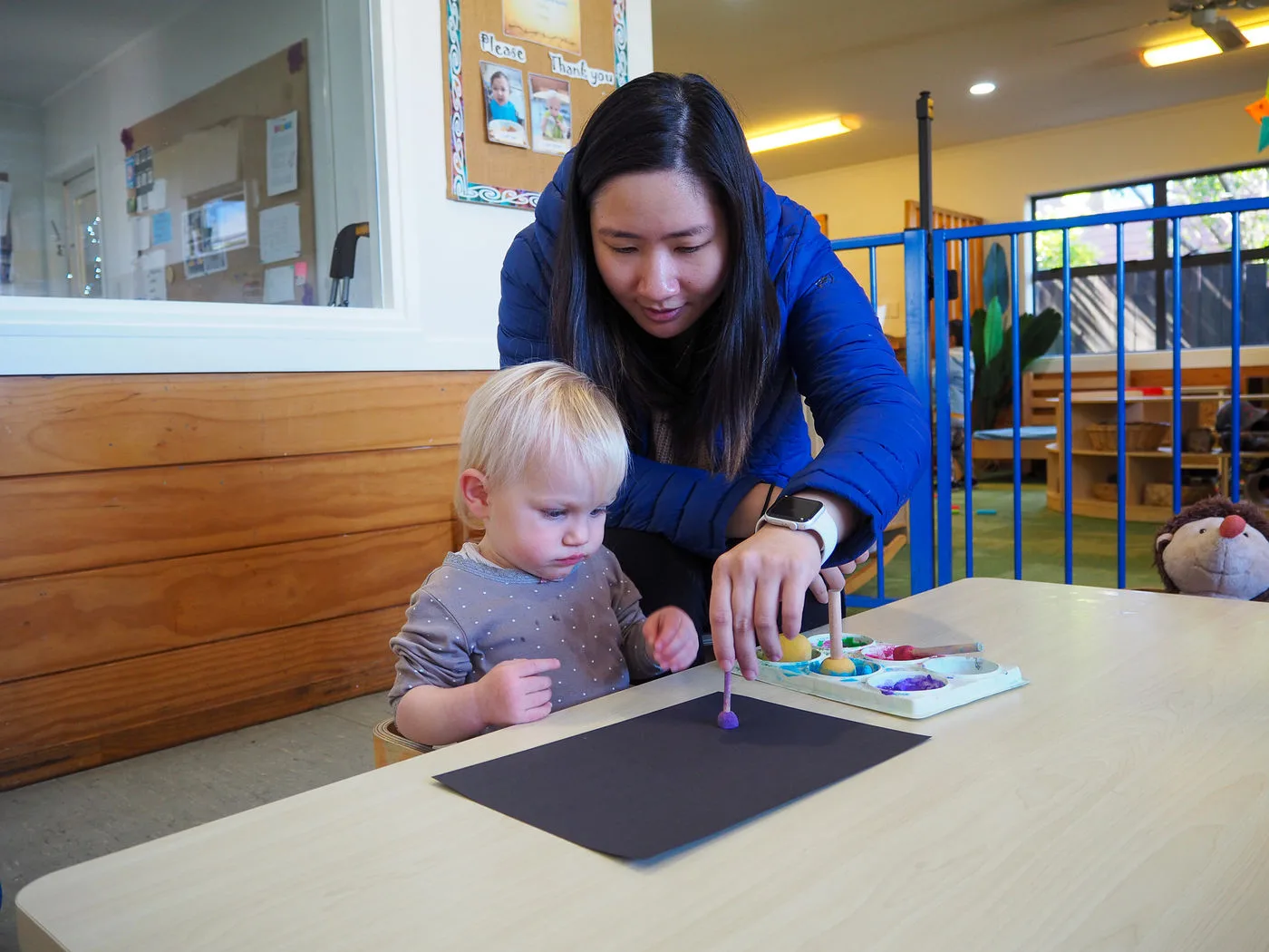 A Growing Minds teacher supporting a toddler with painting at the table