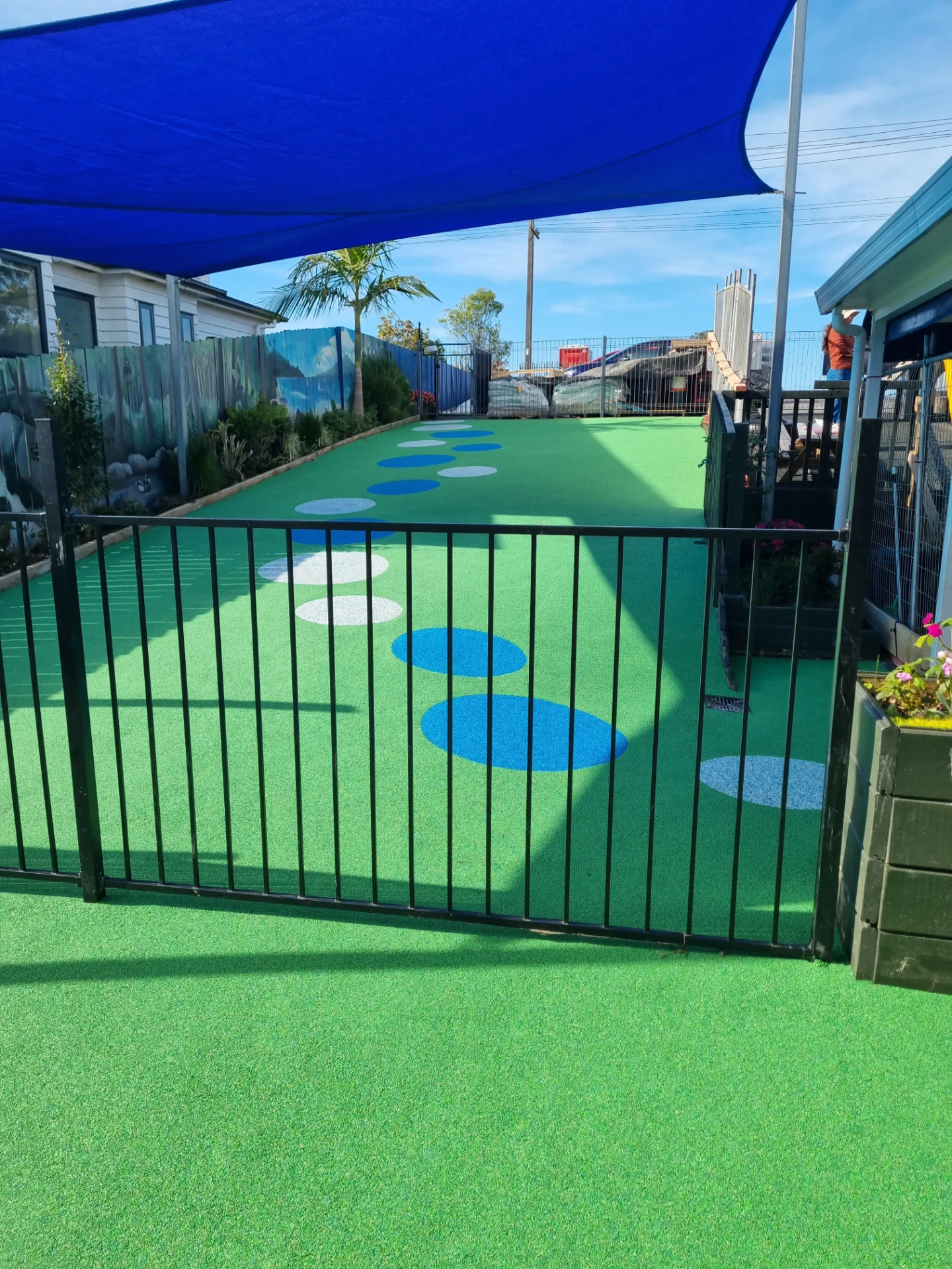 The Growing Minds outdoor playground with soft green turf, shade sail and stepping dots