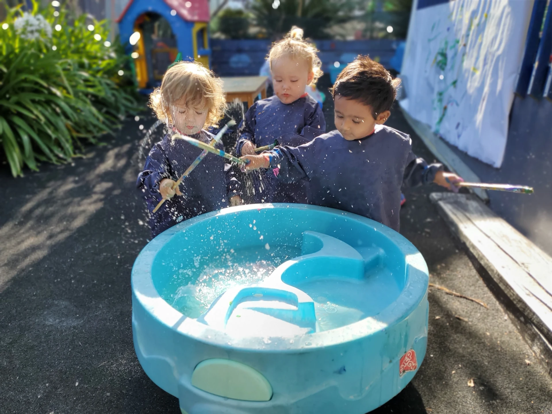 Children splashing and painting with water at the Growing Minds water play trough