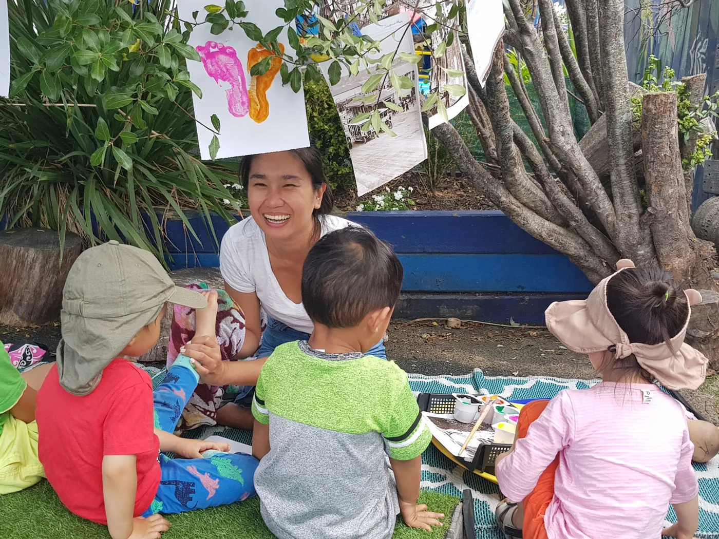 A Growing Minds teacher playing outdoors with children under the shade of the trees