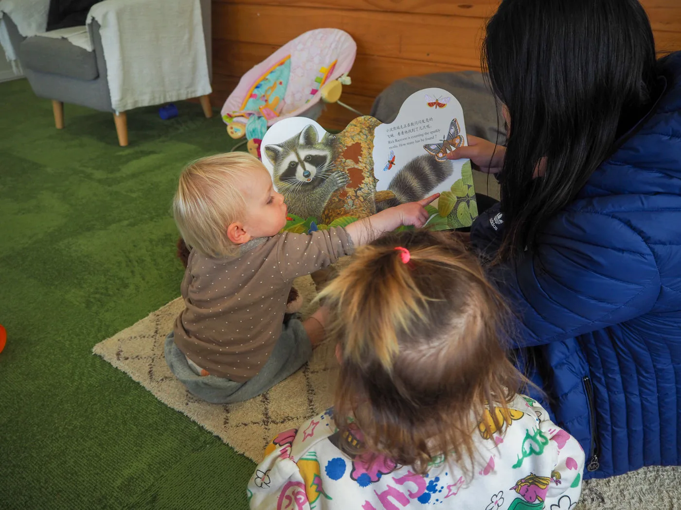 A toddler reading a picture book with a teacher in the Fantail Room at Growing Minds