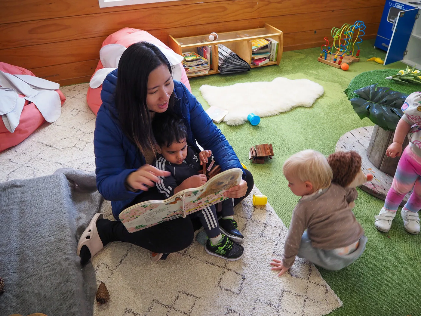 A Growing Minds teacher sitting on the floor reading to babies and toddlers